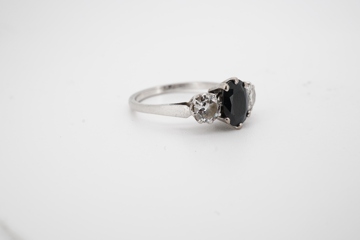 A white metal, single stone sapphire and two stone diamond set ring, the oval cut sapphire approx. 7mm by 5.8mm, the diamonds approx. 0.25ct each, size N.
